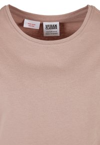 T-shirt rose clair avec un col rond, fabriqué en coton doux. Les étiquettes comportent des instructions d'entretien et le nom de la marque "Urban Classics".