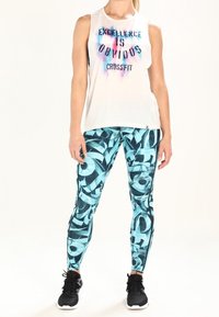 Biała koszulka bez rękawów z napisem „EXCELLENCE IS OBVIOUS CROSSFIT” w kolorze niebieskim i różowym. Niebieskie legginsy z abstrakcyjnymi wzorami. Czarne buty sportowe.