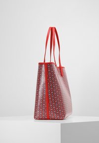 Przezroczysta torba na ramię z czerwonymi skórzanymi uchwytami, ozdobiona geometrycznym wzorem w kolorze czerwonym, niebieskim i białym. Strukturalny kształt z kontrastowymi wykończeniami.