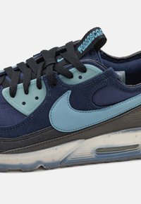 Modré a černé sportovní boty s textilním svrškem, gumovou podešví, Air Max odpružením a kontrastními světle modrými akcenty na logu a dírkách pro šněrování.