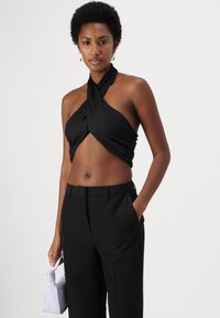 Mustmustatud halter-top, millel on keeratud eesmine detail, ühilduvatel mustadel pükstel. Mudel hoiab käes väikest lavendlite värvi käekotti.