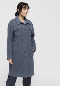 Abrigo de mezcla de lana, gris oscuro, con cuello, cierre de botones en la parte delantera, dos bolsillos en el pecho y bolsillos laterales; tejido suave y texturizado.