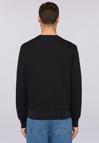 Svart crewneck sweatshirt med texturerad yta, ribbade ärmslut och fåll, parat med ljusblå denimjeans.