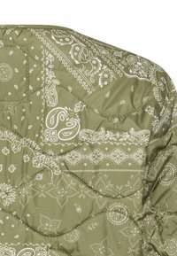 Polstret jakke i olivengrøn farve med et hvidt paisley-mønster og quiltet tekstur. Fremhævet med dekorativ syning og en glat finish.