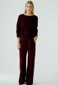 Pull en maille bordeaux avec un motif en vagues, associé à un pantalon large assorti avec des rayures latérales. Tissu texturé avec une coupe décontractée.