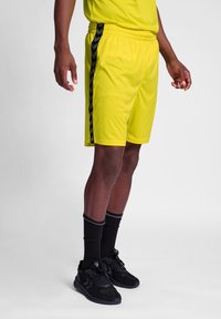 Helle gelbe Sportshorts mit schwarzem Chevronside-Muster, elastischem Bund und glatter Textur. Getragen mit schwarzen Socken und Sneakers.