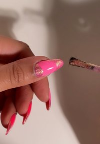 Kloka rosa akrylnaglar med en övertoningseffekt. Änden har guldglitter. En pensel med torkad produkt hålls i närheten.