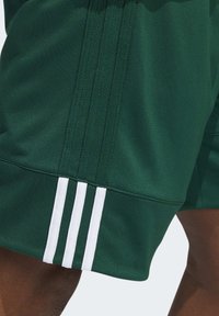Grüne Sportshorts aus strukturiertem Stoff, mit drei weißen Streifen am Saum und einem klaren, schlanken Design.