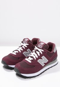 Sneaker New Balance 574 color bordeaux con tomaia in mesh e suede, lacci bianchi, dettagli grigi, collo imbottito e suola in gomma.