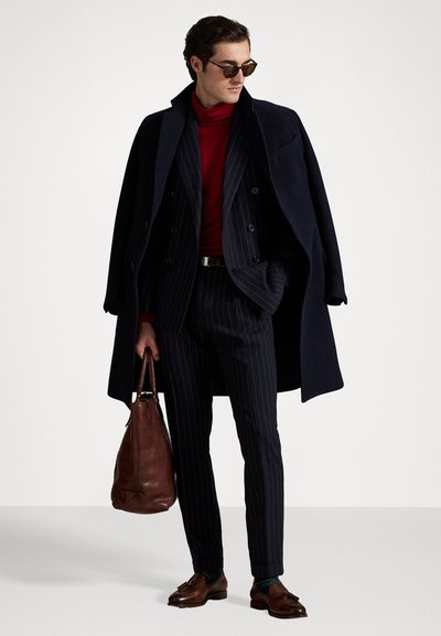 Námornícky vlnený kabát, červený rolák, prúžkovaný oblek, hnedé kožené topánky a taška. Doplnky zahŕňajú slnečné okuliare a opasok.