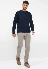 Navyblaues Langarmhemd mit einer Brusttasche, kombiniert mit hellbeigen Hosen und taupefarbenen Wildlederschuhen mit weißen Sohlen.