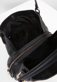 Musta nahkalaukku, jossa on teksturoitu pinta, kultainen vetskari ja sisätasku. Sisäosa on vuorattu mustalla kankaalla.