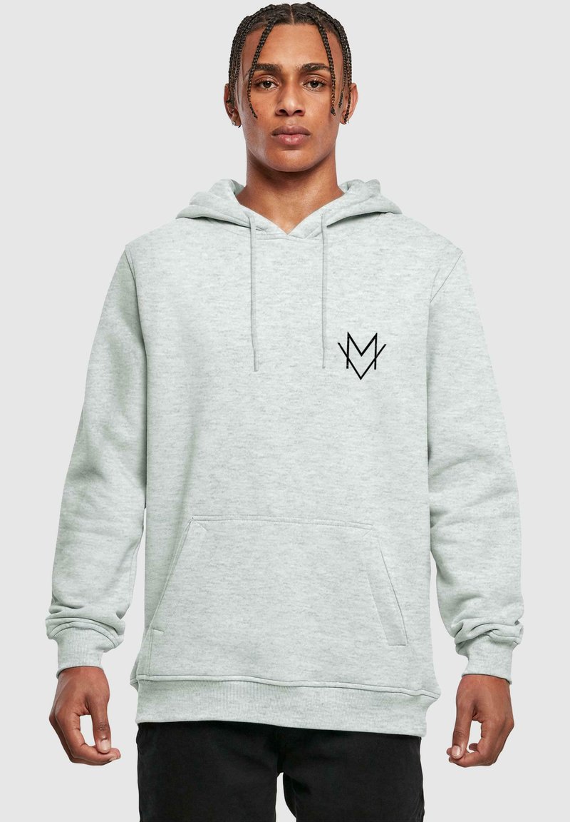 Svetlošedá mikina s kapucňou vyrobená z mäkkej látky, s šnúrkou na kapucni, prednou vreckom a čiernym logom na hrudi. Uvoľnený strih.