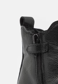 Czarne skórzane botki za kostkę z teksturowanym wykończeniem, bocznym zamkiem błyskawicznym i małym uchwytem na górze dla łatwego zakładania.