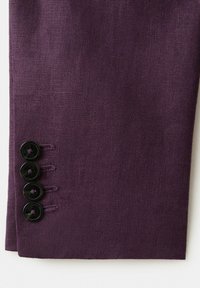 Manchon en tissu violet avec quatre boutons noirs cousus très près les uns des autres près du poignet.