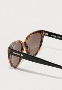 Kassi silmadega päikseprillid, millel on kilpkonnakilbiga raam ja pruunid objektiivid. Omaduseks on must vars, millel on "LOVE MOSCHINO" ja väike südameaktsent.