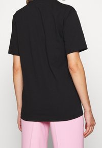 Camiseta de algodón negra de manga corta, con un sencillo cuello redondo y un corte relajado. La vista trasera muestra líneas limpias y sin detalles adicionales.