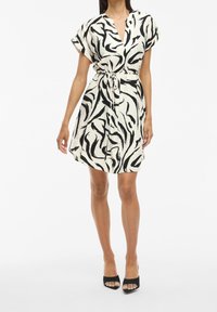 Vestido de manga corta, hasta la rodilla, con un patrón abstracto en blanco y negro, hecho de tejido ligero, que cuenta con un cinturón ajustable en la cintura.