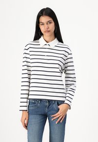 Long-sleeve polo shirt in white with navy stripes, featuring a collared neckline and button placket. Paired with blue jeans.