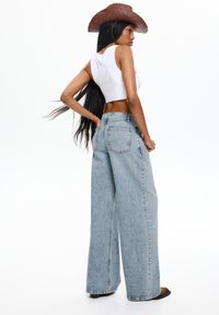 Light blue wide-leg jeans made of denim, featuring a high waist, front and back pockets, paired with a white crop top and a brown straw hat.