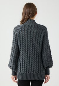 Maglione lavorato a maglia grigio scuro con motivo a trecce, maniche oversize, colletto alto e orlo a coste. Senza chiusure visibili.