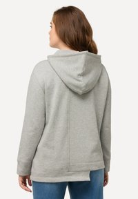 Felpa grigia con un fit rilassato, texture morbida e cappuccio con lacci. Presenta un dettaglio di cucitura sul retro e polsini a costine, abbinata a jeans blu.