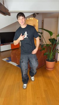 Svart grafisk t-skjorte med et fargerikt trykk, kombinert med grå cargobukser. Personen har på seg sølvfargede joggesko og står i en stue.