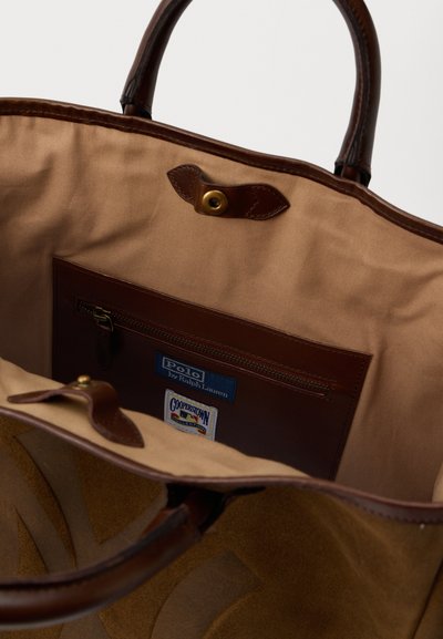 Interior de um saco tote castanho com um forro de tecido suave, apresentando um bolso com fecho éclair e detalhes em pele, incluindo um fecho de botão e um detalhe de marca.