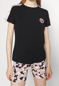 Czarna bawełniana koszulka z krótkim rękawem i różowym logo, w zestawieniu z wzorzystymi szortami z różowymi i beżowymi plamami na czarnym tle.