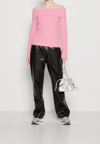 Różowy sweter o odkrytych ramionach połączony z błyszczącymi czarnymi skórzanymi spodniami oraz małą srebrną torebką na sznurek. Noszone są sneakersy z szarymi akcentami.
