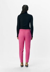 Un haut noir à manches longues ajusté associé à un pantalon rose en stretch avec une taille et des poches arrière, porté avec des sandales à talons noires.
