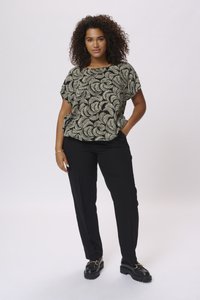 Blouse à motifs noir et crème à manches courtes, assortie à un pantalon noir et des chaussures noires épaisses, le mannequin pose devant un fond clair.