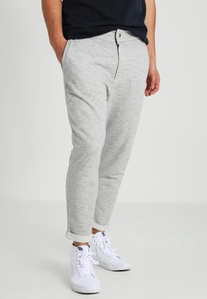 Homme portant un pantalon slim gris clair retroussé aux chevilles et des baskets montantes blanches, debout avec une main dans la poche.