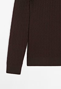 Tmavě hnědý pletený svetr s texturovaným vzorem copánků, žebrovanými manžetami a lemem. Látka působí měkce a pružně.