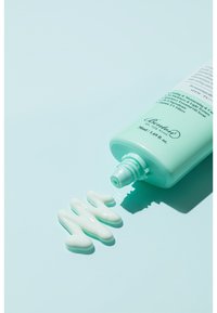 Ljusgrön tub av hudvårdsprodukt med skruvkork, med en slät, krämig vit textur som spillt bredvid på en ljus bakgrund.