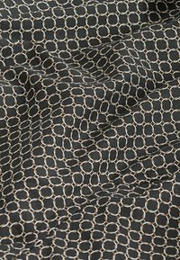 Tissu noir avec un motif géométrique de hexagones entrelacés en crème et marron clair, présentant une texture lisse et un éclat.