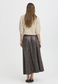Jupe longue en satin gris foncé avec une texture lisse et une taille élastique, associée à un pull court à manches courtes beige clair et texturé.