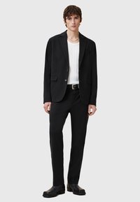 Black blazer with two buttons, paired with a white ribbed shirt and black trousers. Smooth fabric, clean lines, minimalistic design, black footwear.