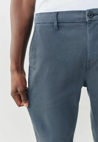 Tengerészkék nadrág sima anyagból, szabványos derékrésszel, elején zsebekkel és egy gombos záródással. Vékony szabású kialakítás.