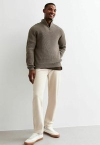 Pullover sweater in taupe knit with a half-zip collar, paired with beige pants and white sneakers with beige accents. Smooth texture and relaxed fit.