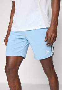 Pantalones cortos deportivos de color azul claro, fabricados con tejido transpirable, con un logo en el muslo izquierdo y acentos negros en los laterales. Textura suave, hasta la rodilla.