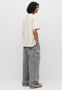 Beige kortærmet skjorte med en afslappet pasform, parret med oversized grå cargo bukser med lommer, denim tekstur og afslappet fodtøj.