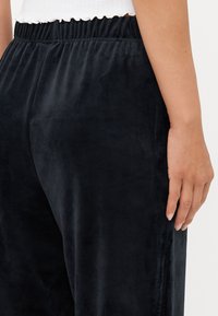 Sorte, myke bukser laget av stoff med elastisk midjebånd. Har en jevn tekstur og en avslappet passform. Ingen synlige mønstre eller detaljer i hardware.