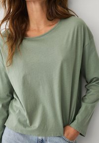 Langärmliges, Rundhals-Shirt aus weichem, leichtem Stoff in einer gedämpften grünen Farbe, mit lässiger Passform und leicht abgerundetem Saum.