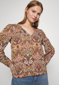 Blusa a maniche lunghe con motivo paisley multicolore in tonalità di marrone, rosso e crema, con scollo a V e tessuto strutturato.