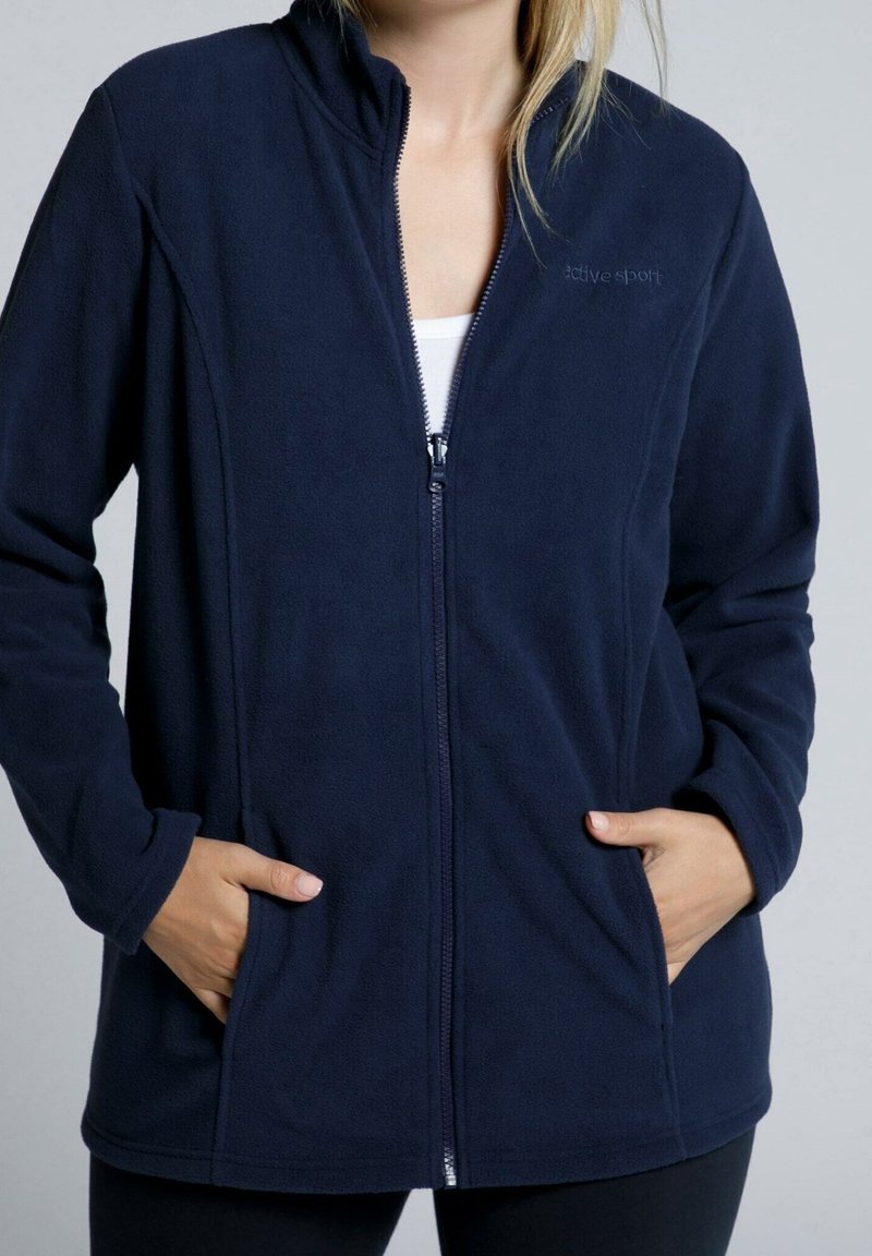 Giacca in pile blu navy con colletto alto, zip frontale completa, tasche laterali e una texture liscia. Caratterizzata dal logo "active sport" sul petto.