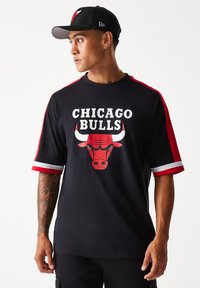 Fekete rövid ujjú póló piros díszítésekkel, "Chicago Bulls" felirattal és egy bika grafikával. Az anyag sima; az ujjakon fehér csíkok találhatók.