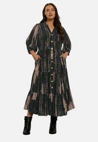 Langes, gestuftes Kleid in Dunkelgrün mit beigen Pinselstrichmustern. Verfügt über eine durchgehende Knopfleiste, einen V-Ausschnitt und Puffärmel sowie seitliche Taschen.