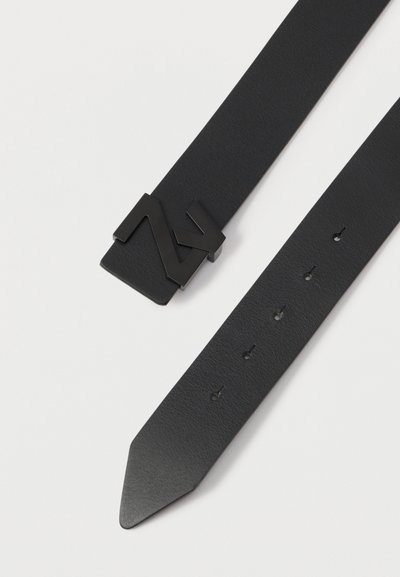 Une ceinture en cuir noir avec une extrémité pointue, dotée d'une boucle en métal noir audacieuse et de plusieurs trous ajustables le long de la sangle.