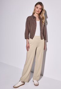 Camicia marrone con bottoni e maniche a tre quarti, canotta bianca, pantaloni beige a gamba larga e sneakers bianche con dettagli beige.